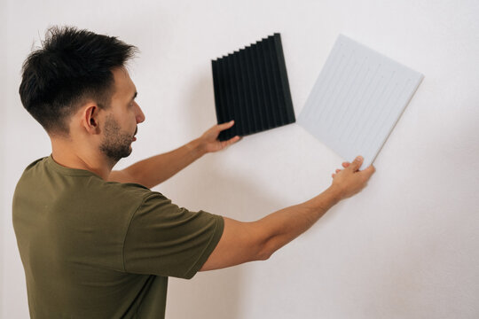 Close-up back view of contractor male choosing between two types of soundproof wall panels, comparing designs and textures while installing for acoustic treatment in room, enhancing sound quality.