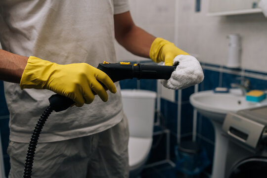 Man wearing yellow rubber gloves holding steam cleaner, preparing to sanitize and deep clean bathroom, focusing on hygiene, domestic chores and household maintenance.