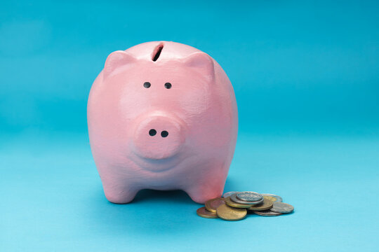 Flat Lay of Piggy Bank Standing Beside Small Pile Various Coins Against Blue Background