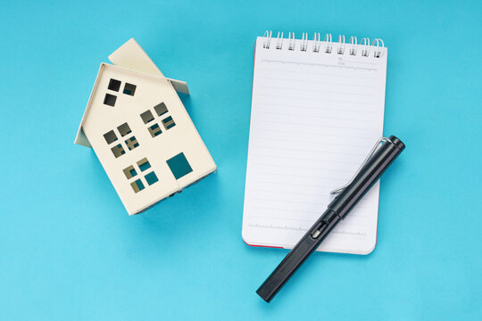 Real Estate Investment Planning with Miniature House and Pen on Notebook Over Blue Background