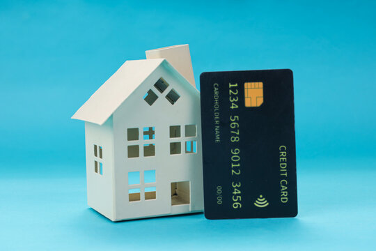 Flat Lay of Credit Card Standing Beside Miniature House Against Blue Background