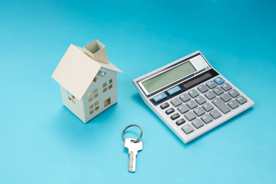 Closeup of Key Between calculator and House Model on Blue Background