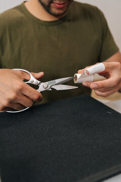Vertical cropped shot of man cutting adhesive medical bandage with scissors, applying first aid to injured finger, caring for wound or minor injury, self-treatment at home or office, close-up.