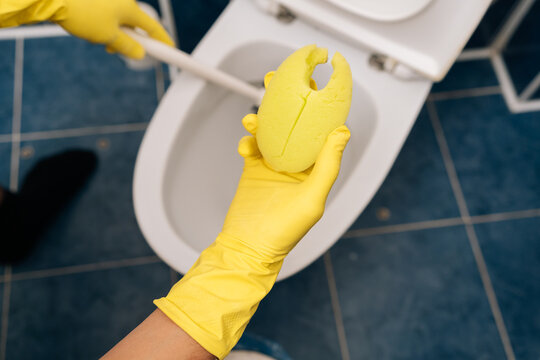 Top view of person in yellow protective gloves cleaning toilet bowl with brush, performing essential sanitary maintenance and daily household chores in home bathroom. Concept of household chores.