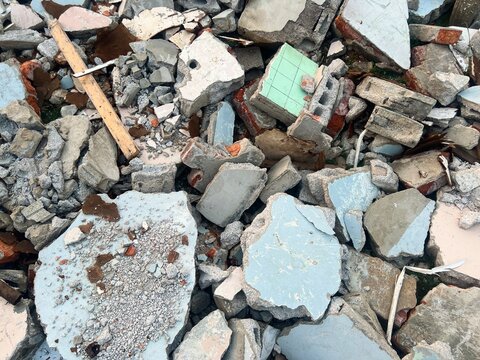 A messy pile of demolition debris consisting of broken concrete blocks, bricks, plaster, and shattered building materials.