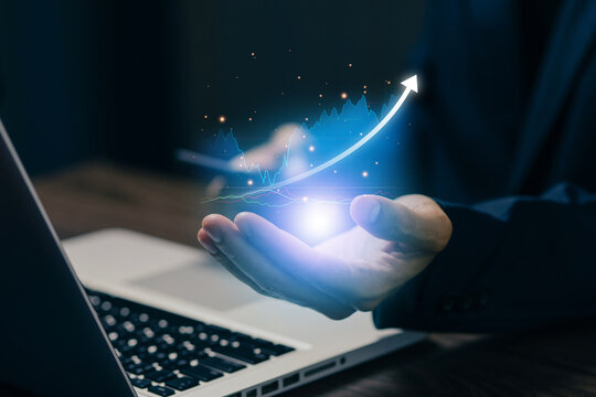 Business professional holding a glowing growth chart above a laptop, representing business analytics, investment performance, revenue growth, strategy, and digital finance technology.