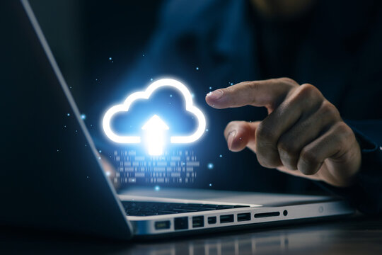 Business professional pointing at cloud upload icon above laptop, representing cloud computing, data backup, file transfer, online storage, digital transformation, and secure technology.
