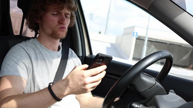 Distracted young driver checks a smartphone while driving through city traffic taking attention away from the road and creating dangerous risks of a serious road accident