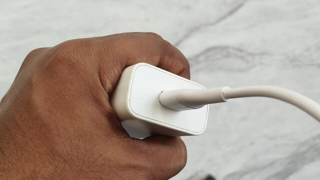 Hand plugging, connecting or input charging cable inside mobile phone or smartphone fast charger adapter usb port hole isolated on white background. Closeup top view.