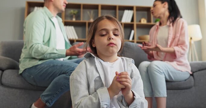 Child watches parents argument at home in fear. Upset child sits near sofa as parents argue, showing family conflict and stress in domestic life. Clear family conflict and stress concept.