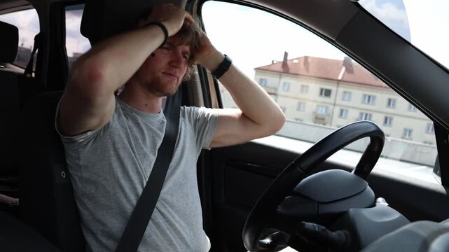 Frustrated young driver has a bad day on the road holding his head in disappointment while stress and problems leave him overwhelmed upset and emotionally exhausted today