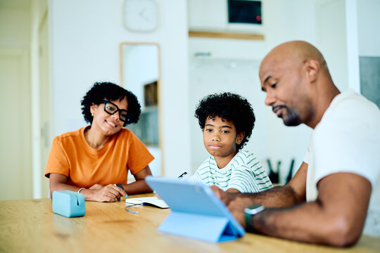 African American parents helping their son with homework using a digital tablet at home, focusing on education and technology