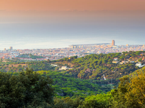 Scenic panoramic aerial view over coastal town of Mataro in Catalonia with green forested hills and calm Mediterranean Sea under warm sunset golden light.