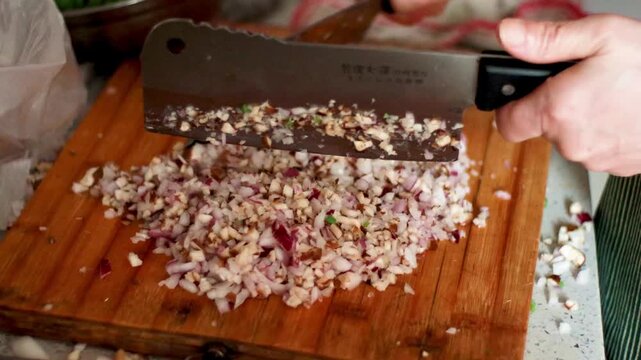 Hands chopping onions and mushrooms on wooden cutting board in kitchen
