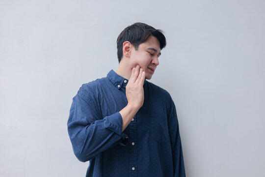 close up young asian man frown and use hand to massage on cheek after feeling pain or hurt from tmj muscle symptom at home for un healthy lifestyle and treatment concept