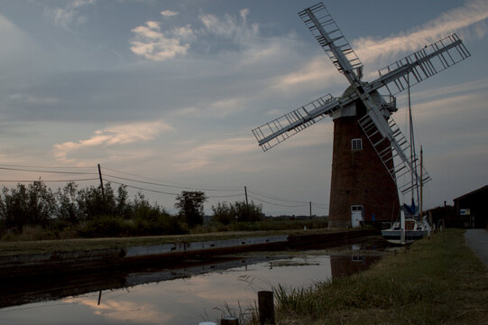Traditional Norfolk windmill beside a rural waterway under an evening sky