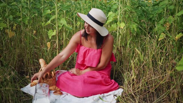 Close up of woman in pink dress enjoying picnic amidst sunflowers with basket bread milk glass and blanket soft natural light outdoor setting sunflower