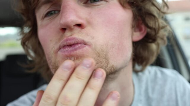 Sparse beard growth on a young mans face shows thin patchy facial hair with uneven density as he touches his cheek and examines areas where beard grows less naturally now