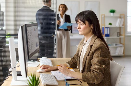 Businesswoman accountant in office using computer spreadsheet. She reviews a financial report, checks data accuracy and updates figures. Focused finance analysis professional portrait concept.