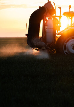 Farmer in tractor spraying crops at sunset