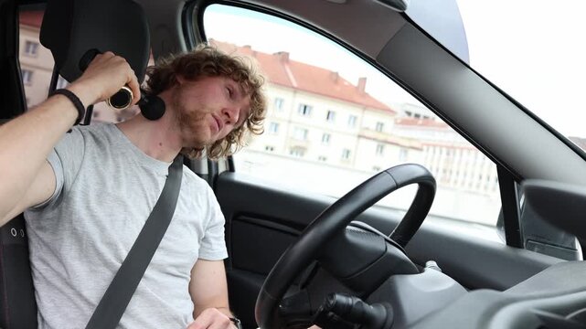 Driver massages his aching neck with a massage gun after long hours on the road relieving soreness and muscle tension caused by extended driving while resting inside his car