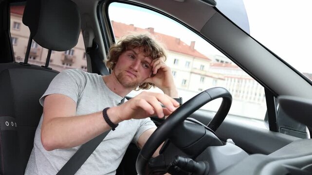 Taxi driver waits without ride requests sitting bored inside his parked car as a slow workday leaves him idle hoping a new passenger booking will finally appear on his app soon