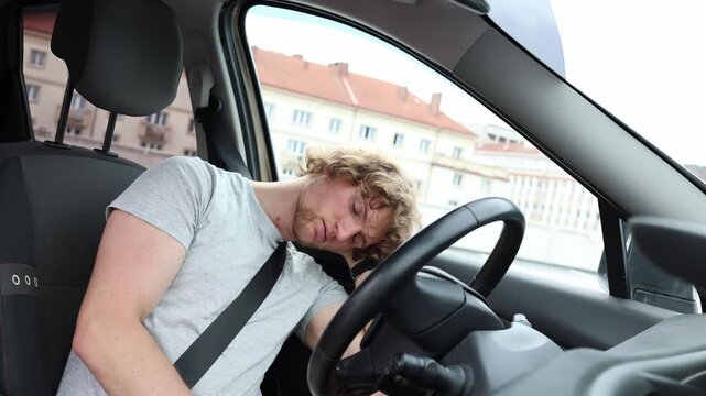 Exhausted young man sleeps in his parked car after a demanding workday unable to continue driving home as fatigue takes over while he rests securely with his seat belt on

