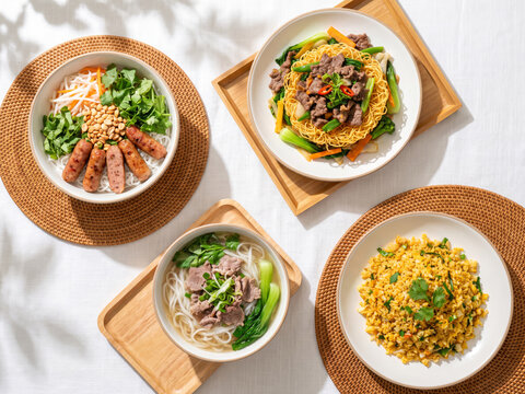 Top view of assorted asian dishes including beef pho noodle soup, fried rice, crispy egg noodles, and rice vermicelli salad on table.