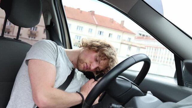 Exhausted young driver falls asleep inside his parked car after work too tired to make it home resting behind the steering wheel after a long and demanding workday alone
