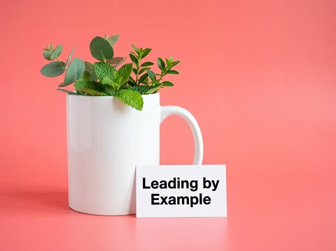 White mug filled with green leaves next to a Leading by Example card ideal for corporate branding symbolizing role modeling and mentorship