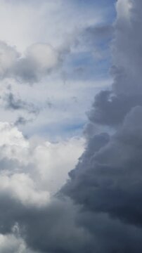 Vertical real-time video of dark clouds rolling in over a blue and white sky.