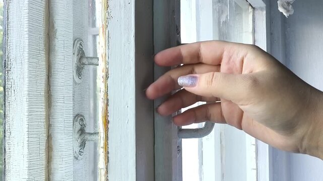 Woman checking for cold drafts coming through gaps in an old wooden window, air leaking through cracks, window sealing and home insulation in cold weather.