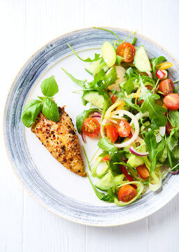 Grilled chicken fillet with vegetable salad on white plate. Top view. 