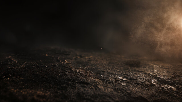 A close-up view shows a dark, textured surface. Light shines from one side, revealing details like cracks and rough spots. The setting may depict a natural scene or a studio backdrop