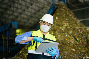Fototapeta premium Quality inspector using digital tablet near conveyor belt and garbage pile inside municipal recycling plant.
