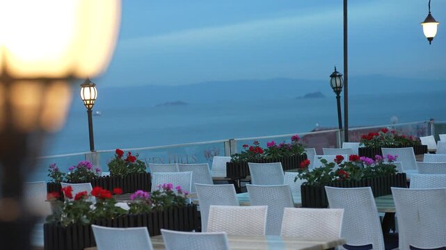 Outdoor rooftop restaurant terrace overlooking the sea at dusk in Sultanahmet Istanbul Turkey. White dining chairs, flower boxes and decorative lamps create a peaceful atmosphere.