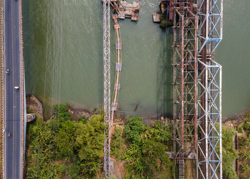 Aerial View of Three Parallel Bridges Carrying Road Traffic, Water Pipeline Infrastructure, and Railway Tracks Across a River in Indonesia. Distinct Transportation Infrastructure, Captured from Above.