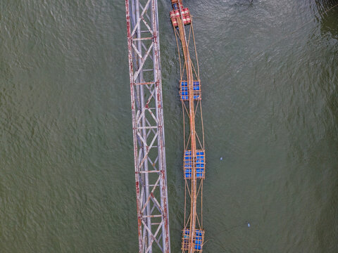 Aerial View of Water Pipeline Bridge Crossing a River Beside a Floating Bamboo Service Bridge Used by Workers in Indonesia, Captured from Above.