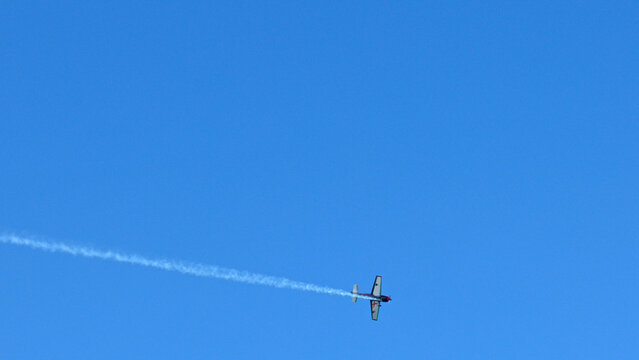 Aerobatic Stunt Plane Performing Maneuvers with Smoke Trail in Blue Sky