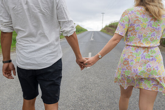 Interracial couple holding hands while walking on a road