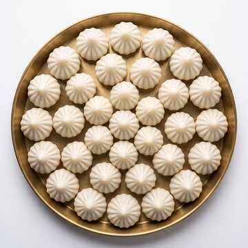 Identical white steamed modaks arranged in a symmetrical radial pattern on a round brass plate