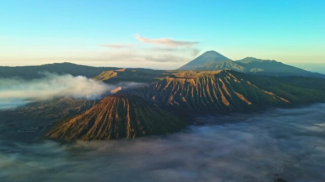 Slow drone approach toward Mount Bromo in vivid morning light, revealing a sea of clouds, Mount Semeru and abundant volcanic smoke across the Tengger caldera, Indonesia