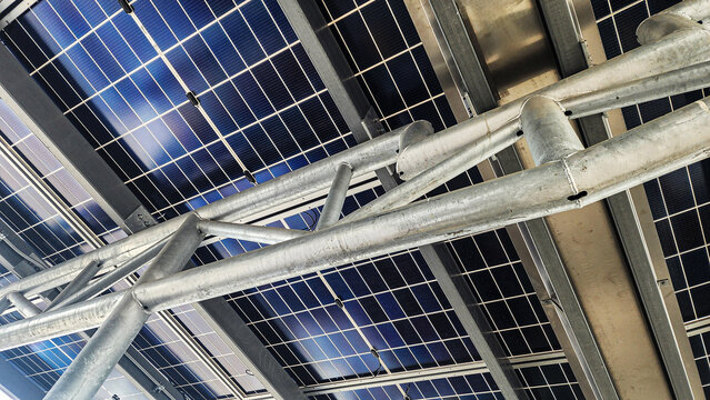 Bottom view of solar panels mounted on steel truss roof structure. Renewable energy canopy installation for commercial building, sustainable infrastructure, and green power technology concept.