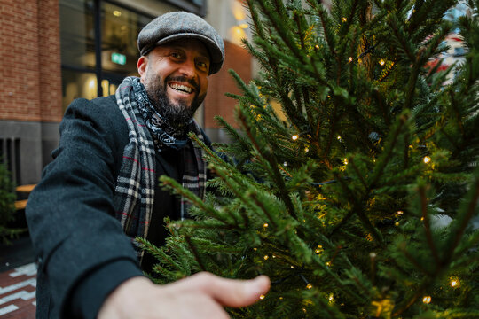 A smiling man in a flat cap greets the camera near a Christmas tree