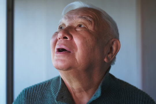 Senior man in green sweater looks up with hope and belief indoors