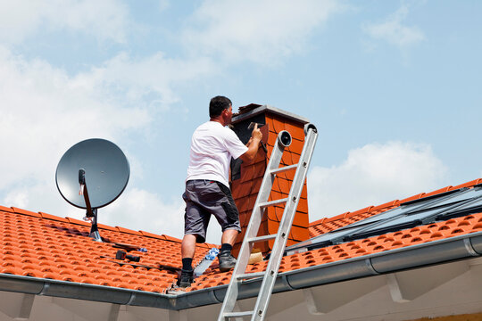 Europe, Germany, Rhineland Palatinate, Man covering chimney with roofing shingles