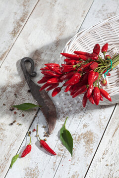 Red chili peppers (Capsicum) in white basket on white wooden table, studio shot