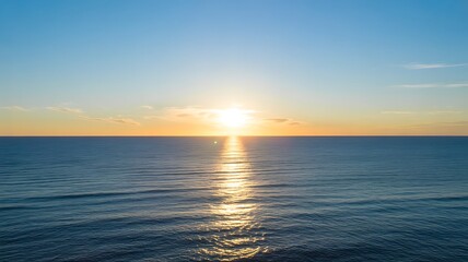 Fototapeta premium Golden sunrise over the calm ocean horizon with soft blue sky and gentle ripples on the water surface during a peaceful early morning landscape view