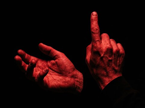 Dramatic red lit hands gesturing in the dark against black background