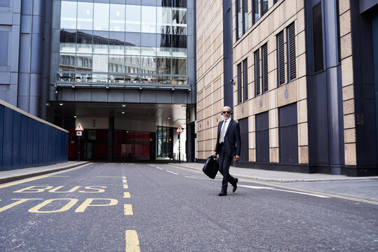 UK, London, senior businessman with headphones crossing the street